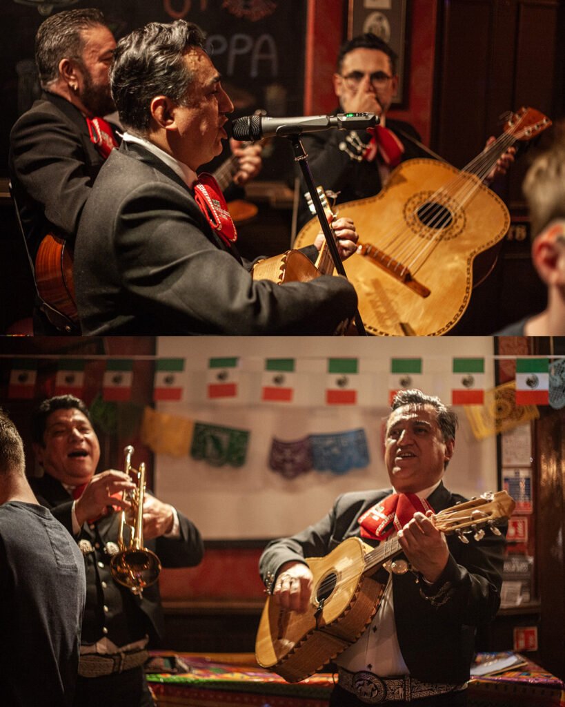 Mariachi singers and guitarists performing under Mexican flags and papel picado at The Bow Bells