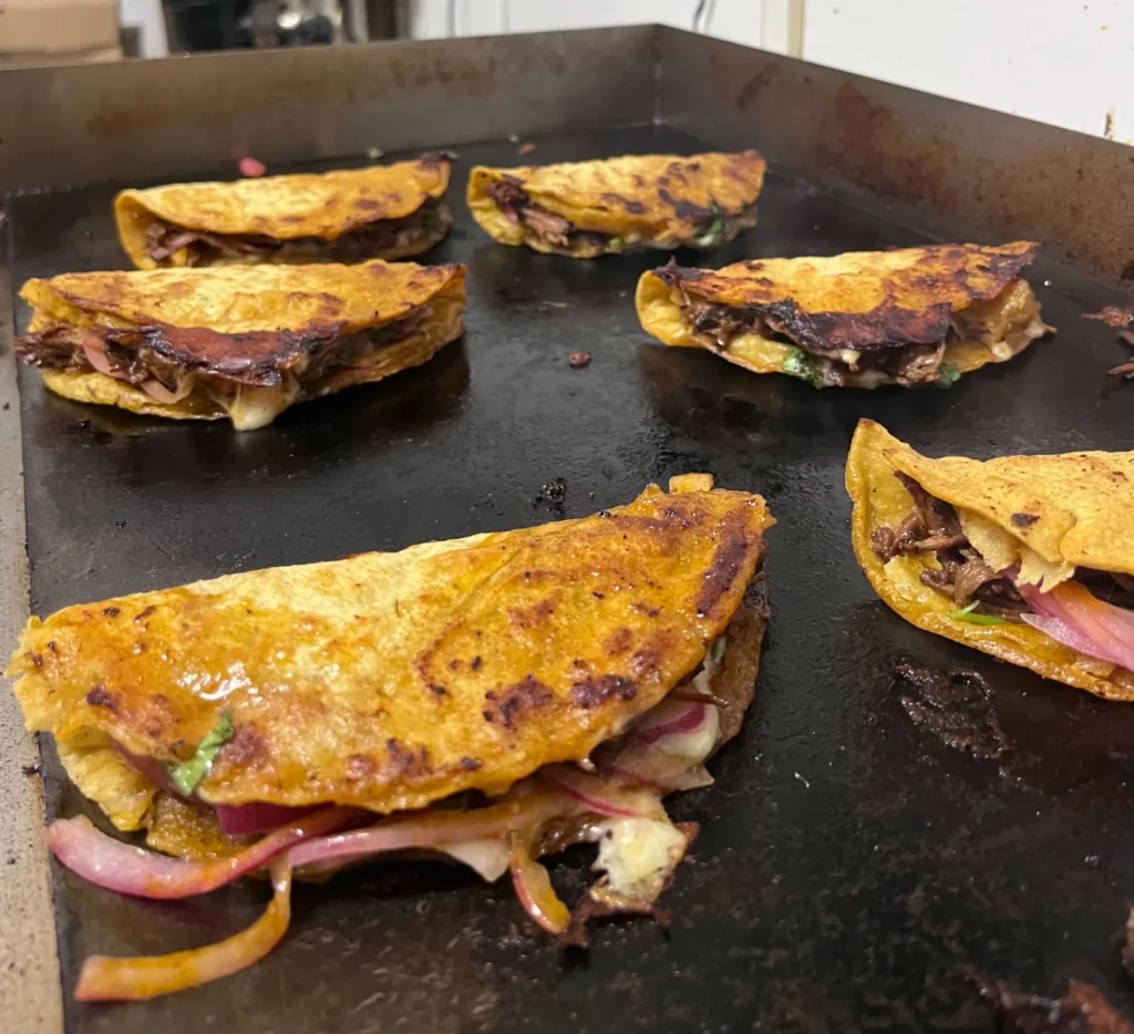 Cheesy beef quesabirria tacos cooking on a flat-top griddle